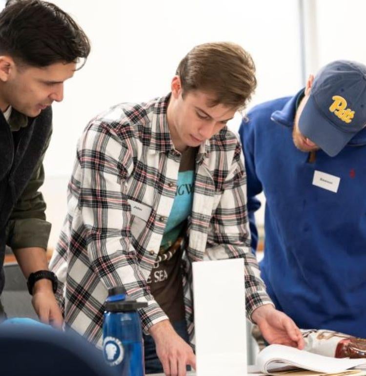Three men standing at a table looking through a packet of papers